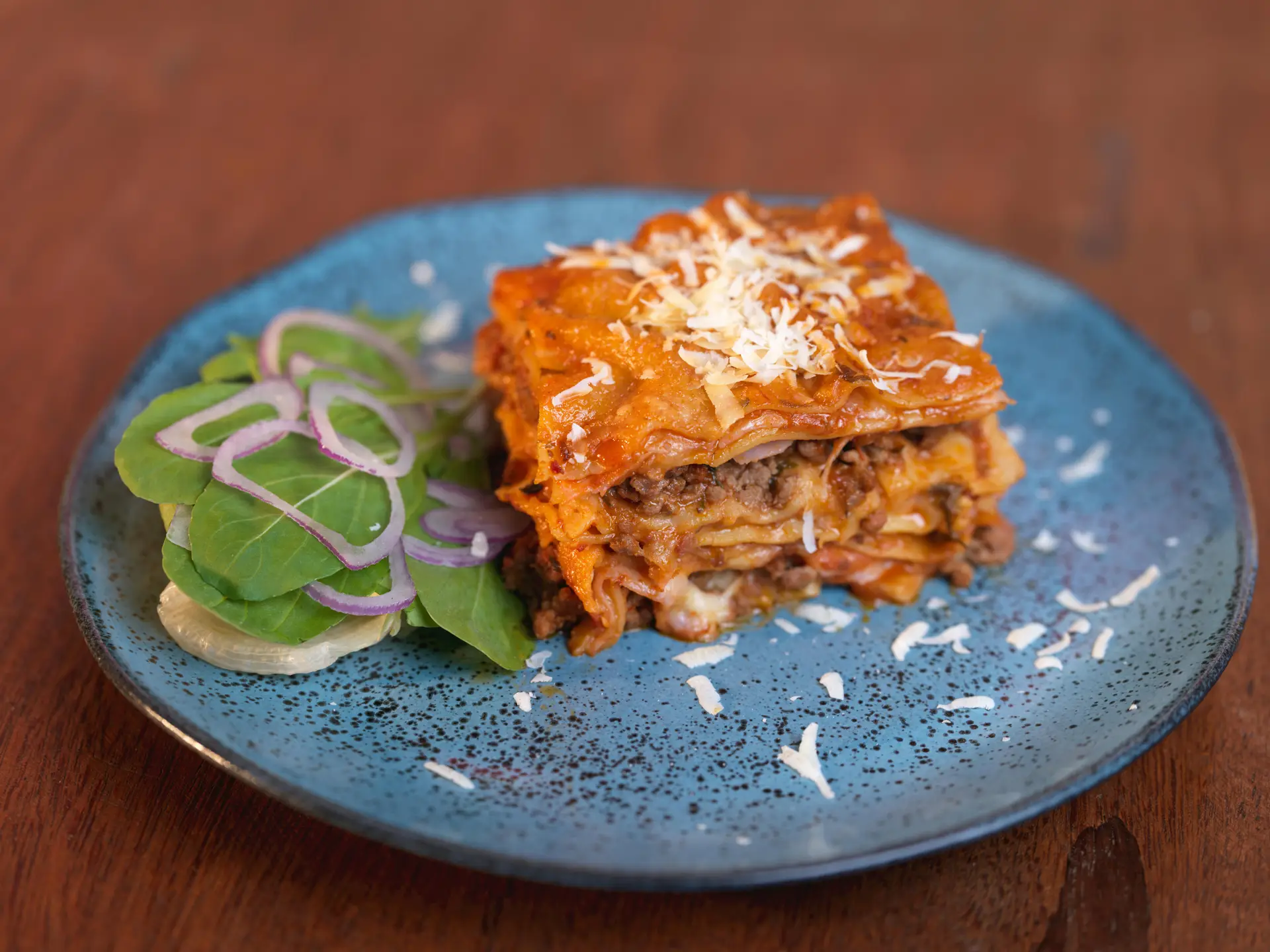 Mouth-watering homemade lasagna with salad served on a rustic blue ceramic plate.